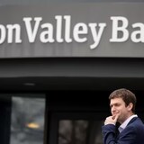 Devant une succursale de la Silicon Valley Bank, un jeune homme en costume sombre a l'air inquiet.