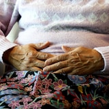 Closeup of an elderly woman resting her hands on her belly.