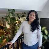 Une femme souriante aux cheveux longs est entourée de plantes.