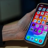 A hand holding a smartphone with an unlocked screen displaying many apps.