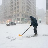 Un homme pellette de la neige dans le centre-ville de Montréal.