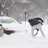 Un homme déblaie la neige autour d'une voiture.