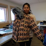 Une adolescente tient devant elle un parka avec un accent de fourrure en août 2022 dans la communauté de Behchoko, aux Territoires du Nord-Ouest.
