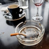 A burnt cigarette in an ashtray next to various glassware and espresson cups.