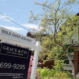 A sold-over-asking sign in front of a brick house.