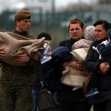 Mujeres y niños cruzan la frontera polaca y son ayudados por un soldado local.