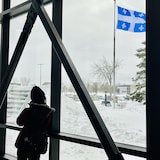 Une étudiante regarde par la fenêtre, où un drapeau québécois flotte.