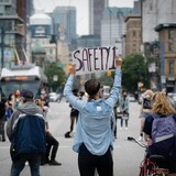People, with their backs to the camera, protest in the street, one person holding a sign above their head.