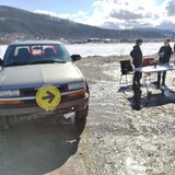 Un bureau de vote installé en extérieur au bord du fleuve Yukon à côté d'une camionnette et trois personnes.