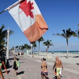 A Canadian flag flies as people walk along the boardwalk in Hollywood, Fla. The number of people moving from Canada to the U.S. hit 126,340 in 2022 — a 70 per cent increase compared to 10 years ago.