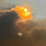 Thick smoke rises towards the skies, veiling the sun.