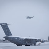 Un avion posé au sol, en hiver et un hélicoptère dans les airs, le 13 février 2023, à Whitehorse, au Yukon.