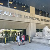 Deux visiteurs en tenues d'été s'approchent de la porte d'entrée de l'hôtel de ville de Calgary. Au-dessus de la porte est écrit Calgary Municipal Building. (Archives)