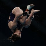 Une athlète de plongeon agrippe ses jambes durant un saut périlleux.