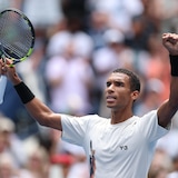 Un joueur de tennis lève les bras avec sa raquette dans la main droite.