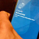 Logo ng ArriveCAN app sa screen ng smartphone na hawak ng isang kamay.