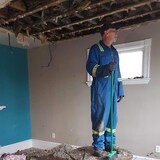 Un homme vêtu d'une combinaison de chantier balaie des débris dans une maison.