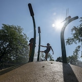 Deux enfants jouent dans une fontaine dans un parc, à la tombée du jour.