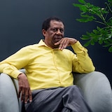 Dany Laferrière prend la pose, assis sur un fauteuil. 