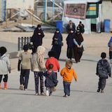 Des femmes voilées et des enfants marchent sur une route à l'intérieur d'un camp de détention. 