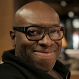 Un homme portant des lunettes sourit à la caméra.