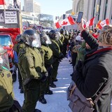 Des policiers portant des casques font face aux manifestants. 