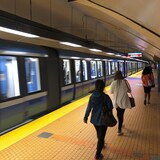 Des gens marchent sur le quai du métro, alors qu'un train passe. 