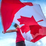 Un jeune garçon qui fait flotter un drapeau du Canada derrière lui.