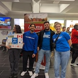 Les quatre étudiants prennent la pose pour la caméra dans un aéroport avec des pancartes de bienvenue.