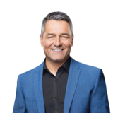 Bruno Savard souriant devant un fond du logo de Radio-Canada.