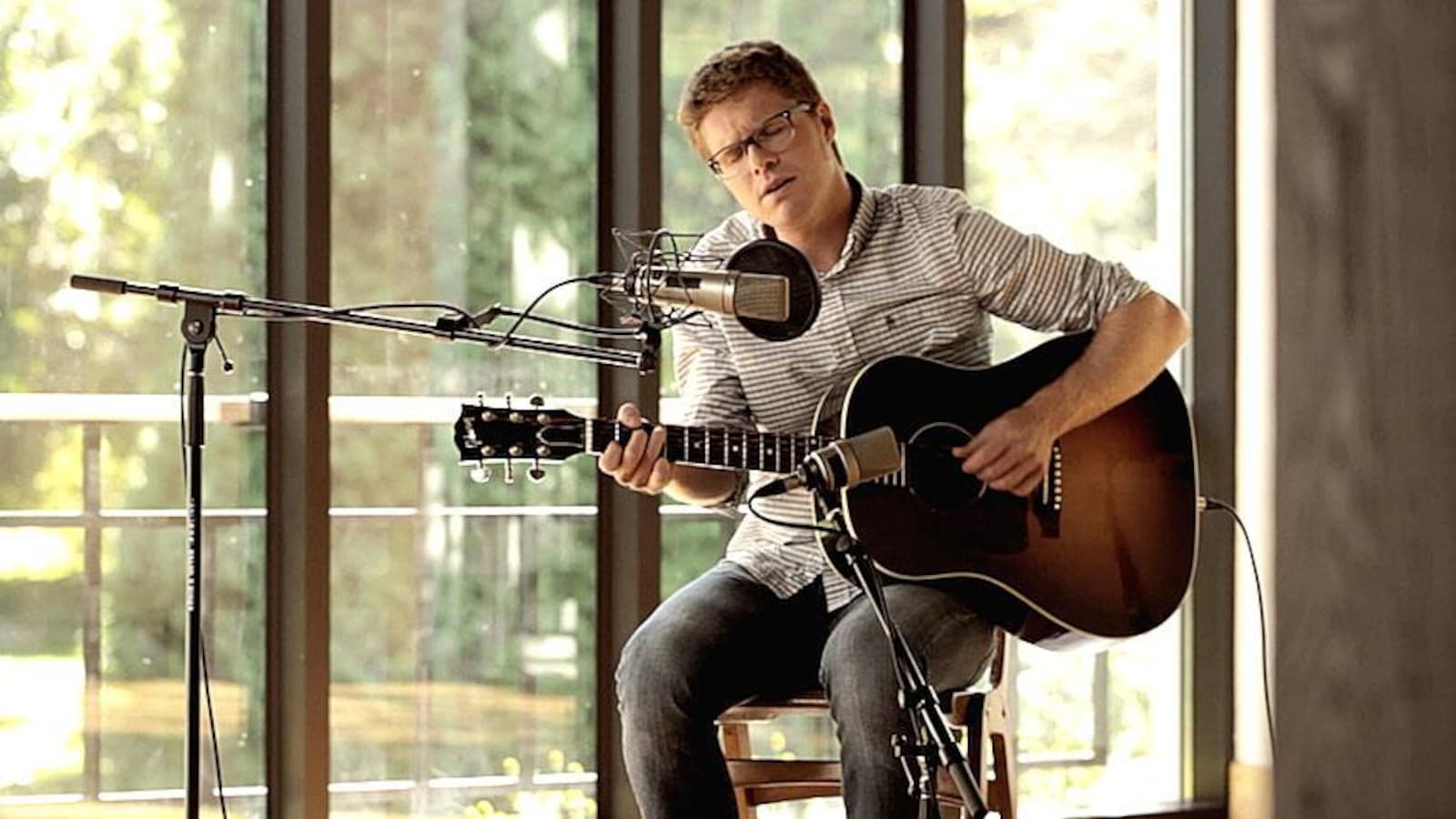 Vincent Vallieres joue de la guitare, assis sur un banc, devant un micro d'enregistrement