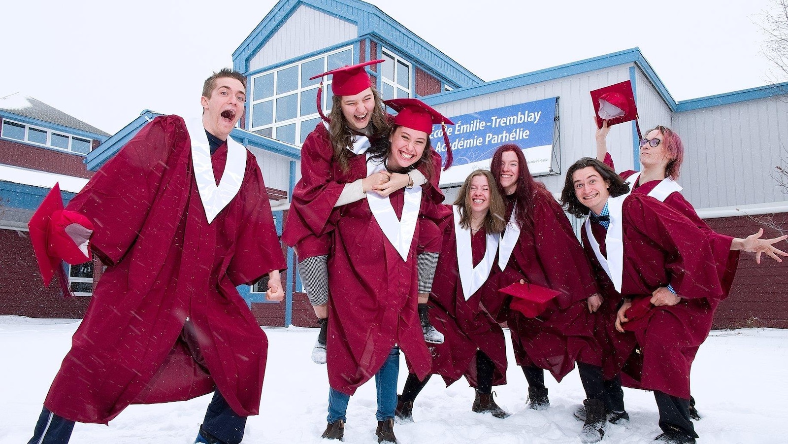 Les finissants en toge qui jouent dans la neige, devant leur école.