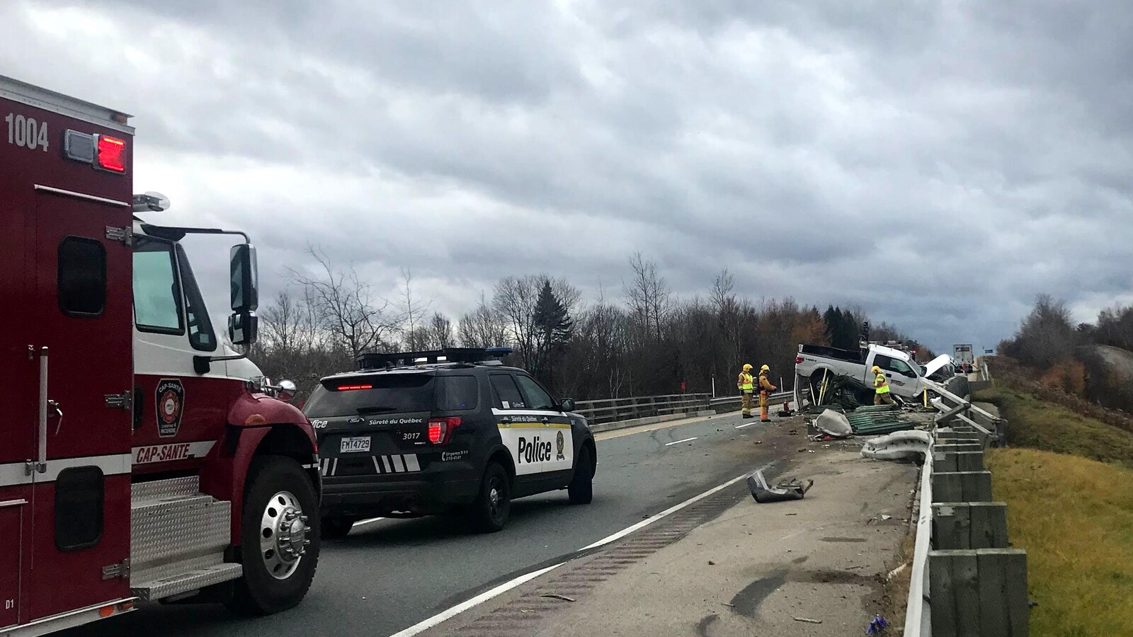 Photo de la scène d’accident. On aperçoit une camionnette blanche accidentée. Un véhicule utilitaire sport de la Sûreté du Québec et un camion de pompier.