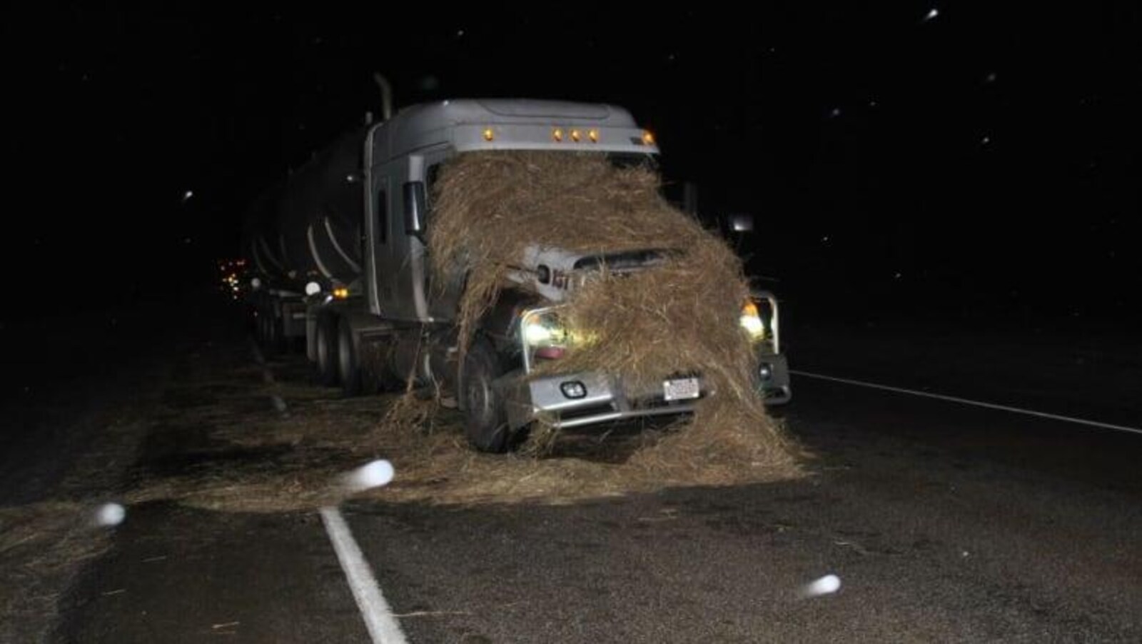Un ballot de paille écrasé sur le devant d'un camion semi-remorque arrêté sur une autoroute.