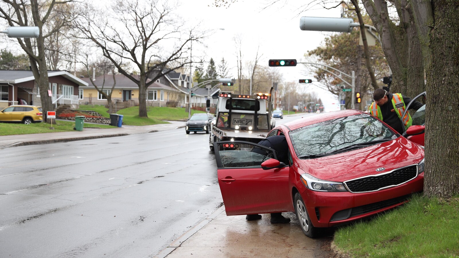 Une voiture rouge de marque Kia est immobilisée après avoir percuté un arbre. L’opérateur d’une dépanneuse s’apprête à remorquer le véhicule.