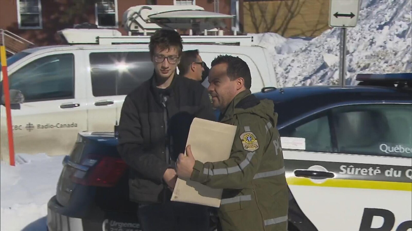 Un jeune homme est menotté et il est accompagné d'un policier de la Sûreté du Québec.
