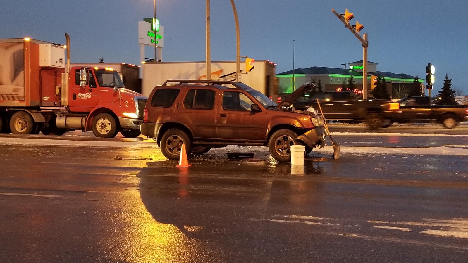Une voiture arrêtée avec le capot levé et des cônes tout autour près d'une intersection.