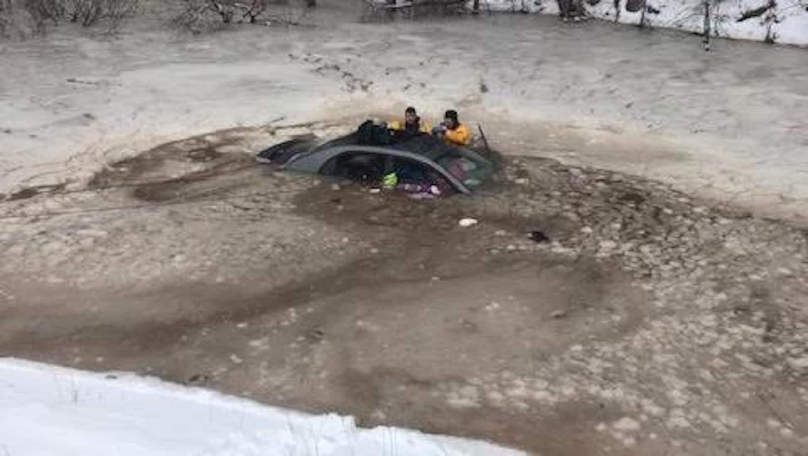 Trois pompiers dans l'eau glaciale jusqu'à la poitrine examinent la voiture immergée.