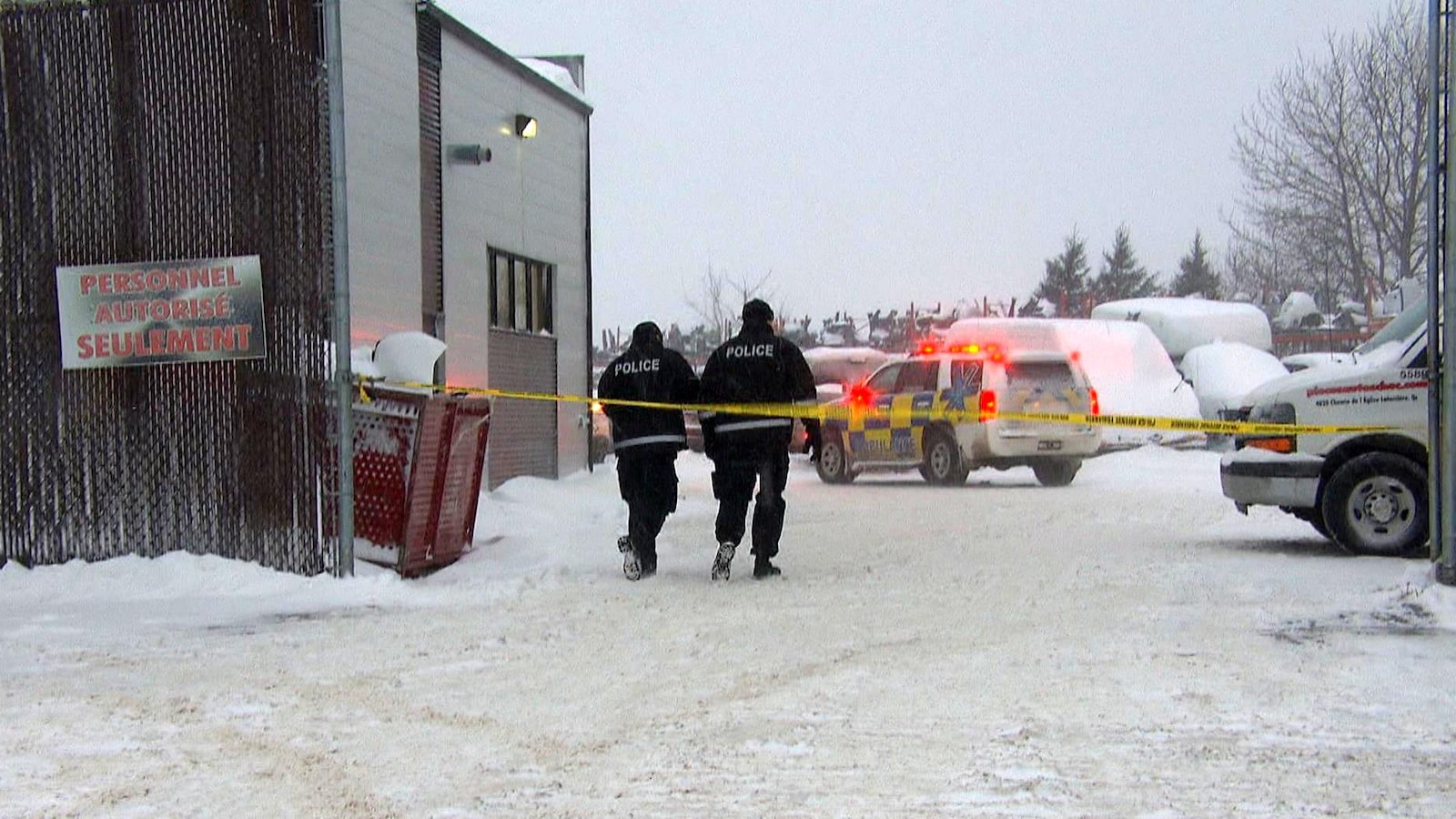 Deux policiers marchent dans la neige près de l'édifice de Pièces d'autos Choc.