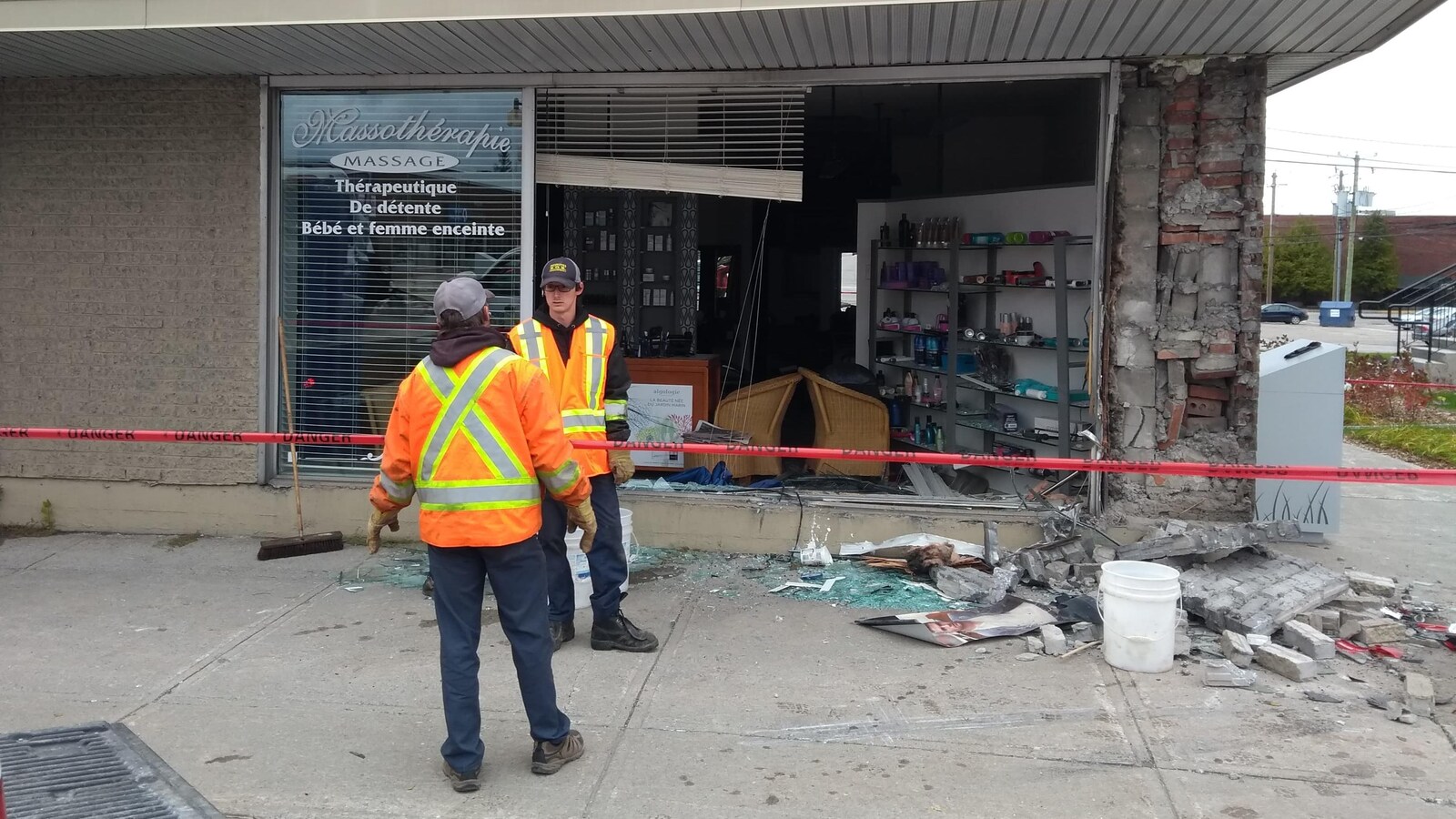 Deux hommes se tiennent devant la vitrine d'un magasin complètement fracassée avec des débris partout sur le trottoir.