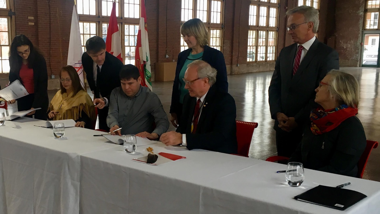Des femmes et des hommes assis à une table signent un document.