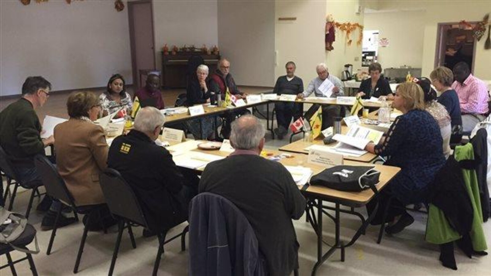 Quinze personnes sont assises autour de tables placées en carré et couvertes de documents.