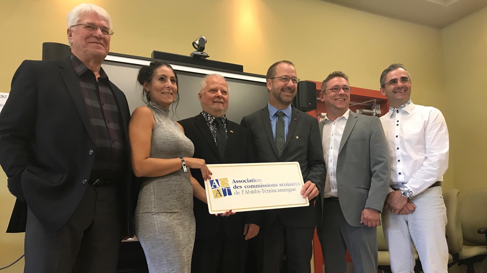 Cinq hommes et une femme sourient à la caméra en tenant une affiche de l'Association des commissions scolaires de l'Abitibi-Témiscamingue.