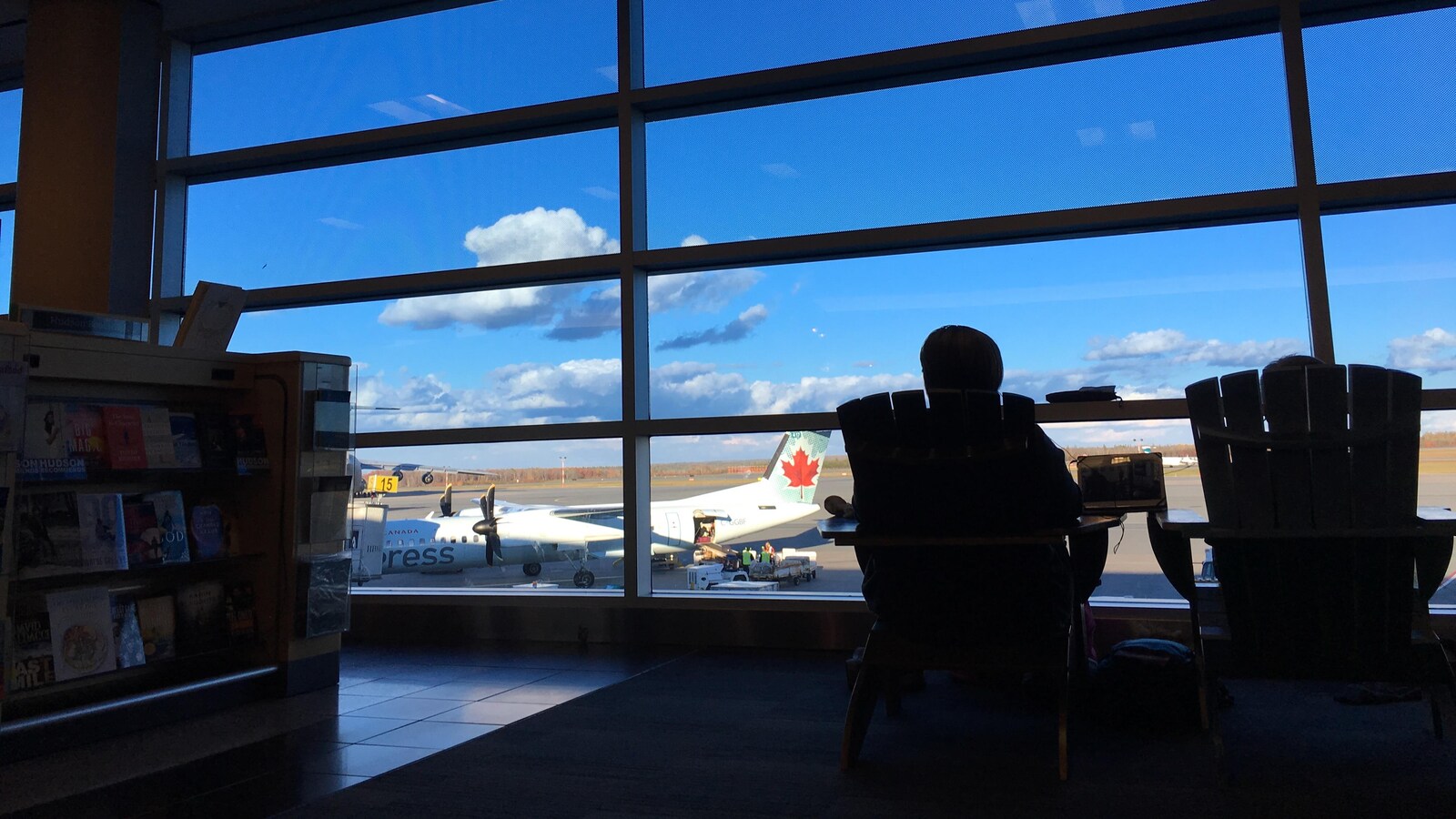 Un passager attend à l'aéroport devant une fenêtre où l'on aperçoit un avion sur la piste.