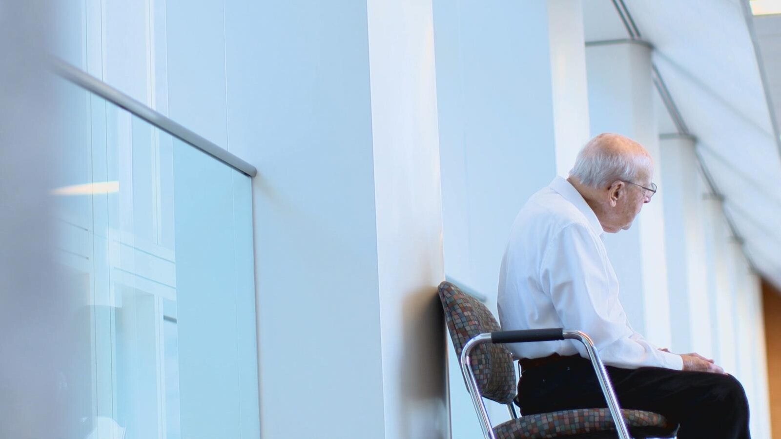 Un homme âgé assis sur une chaise dans un corridor d'hôpital.