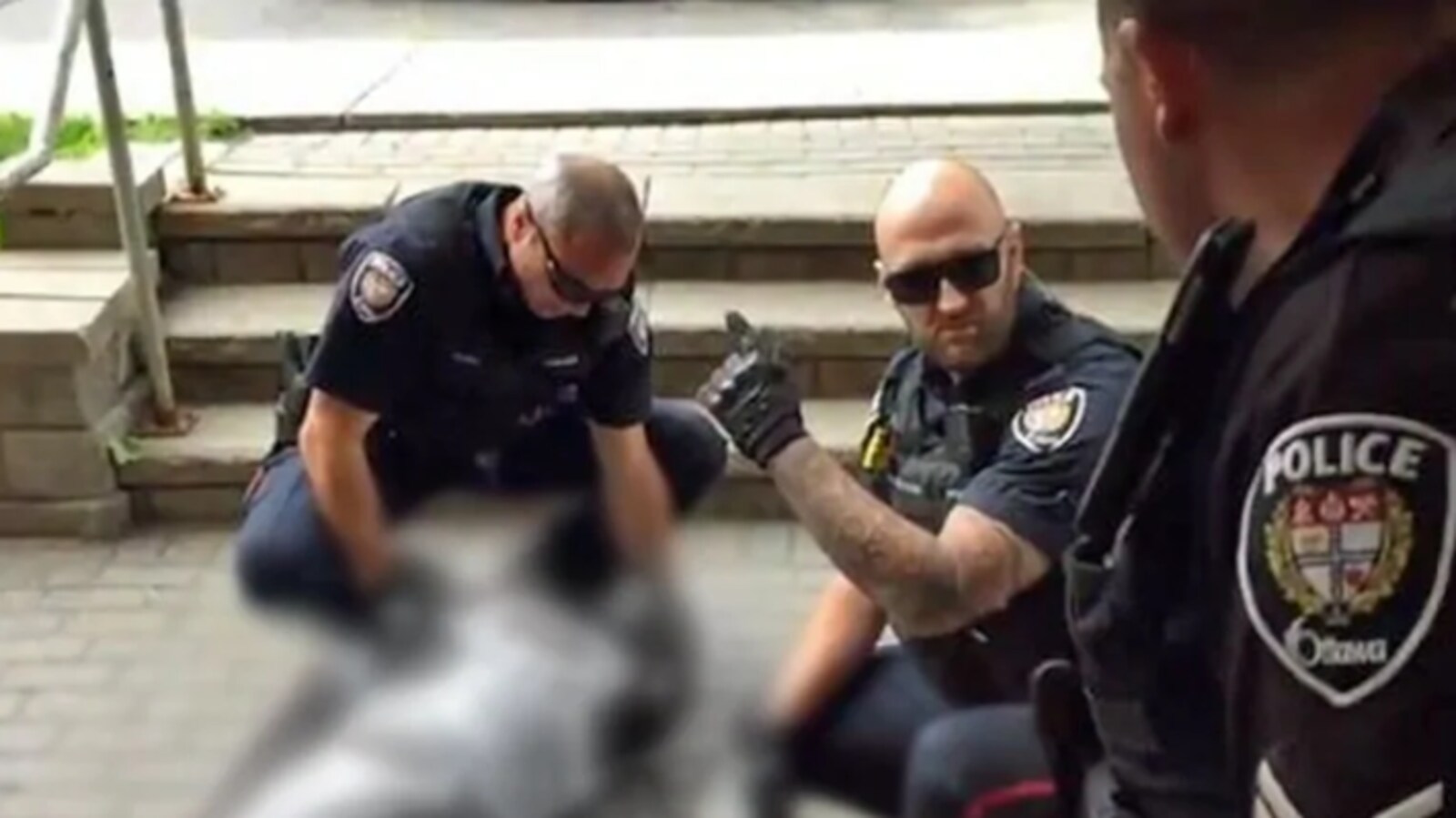 Trois agents de police autour d'un homme étendu par terre. L'image de l'homme au sol a été volontairement brouillée.