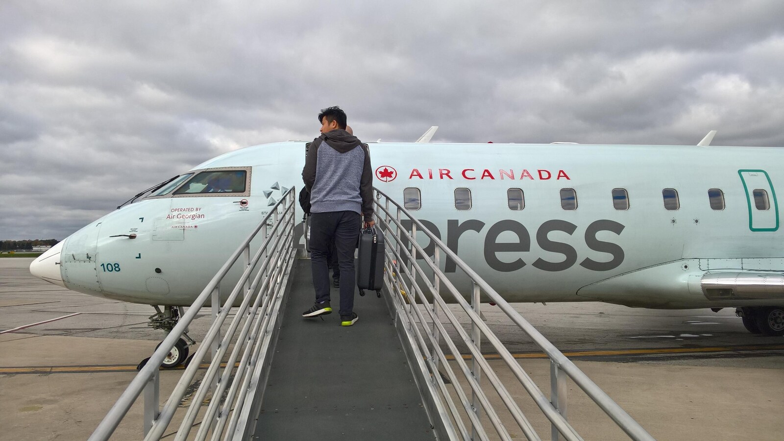 Un passager tenant une petite valise à la main marche le long d'une passerelle avant de monter dans un avion d'Air Canada à destination de Toronto.
