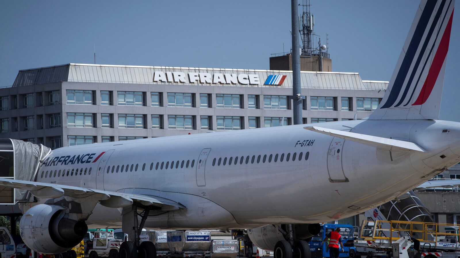 Un avion sur lequel on peut lire « Air France » est posé au sol près d'un bâtiment sur lequel il est aussi inscrit « Air France ».