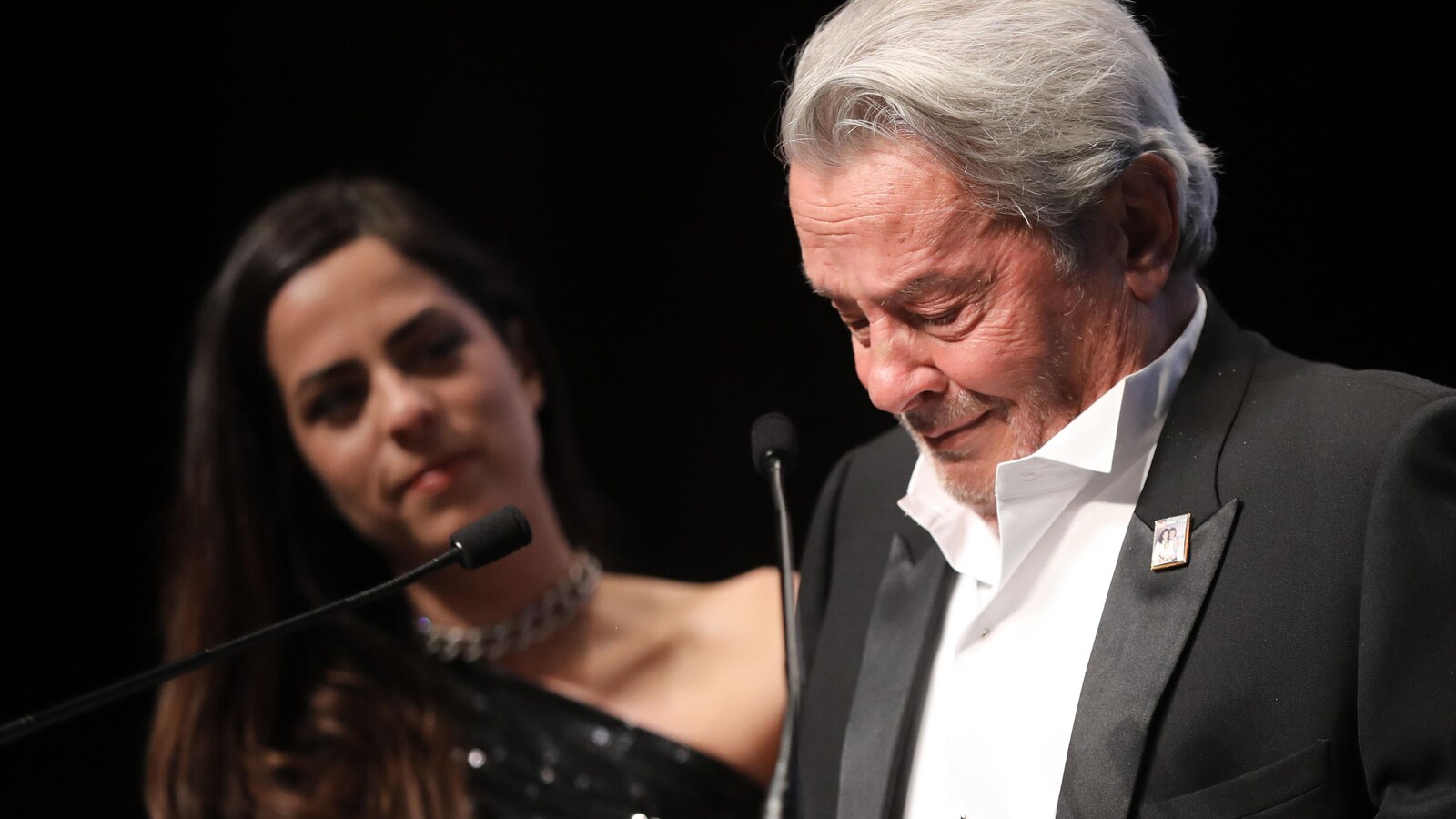 L'acteur Alain Delon, en larmes, devant un micro, après avoir reçu une Palme d'or d'honneur au Festival de Cannes. On aperçoit sa fille Anouchka derrière.