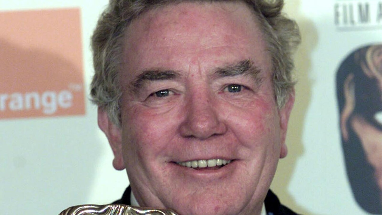L'homme sourit et tient un trophée en forme de visage.